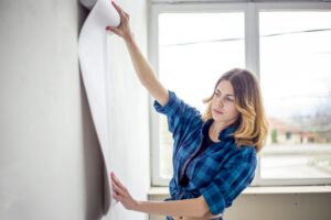 Woman choosing wallpaper and holding it up to the wall.