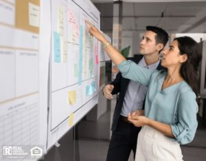 Two analysts engaged in focused discussion in front of large whiteboard filled with diverse sticky notes.