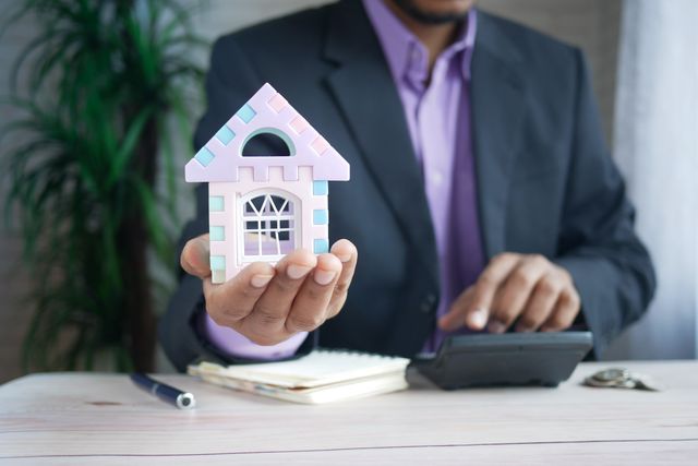 person in a suit holding a miniature house