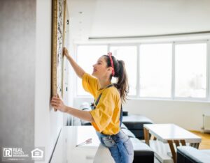 A woman happily hanging a picture on the wall of her rental home.