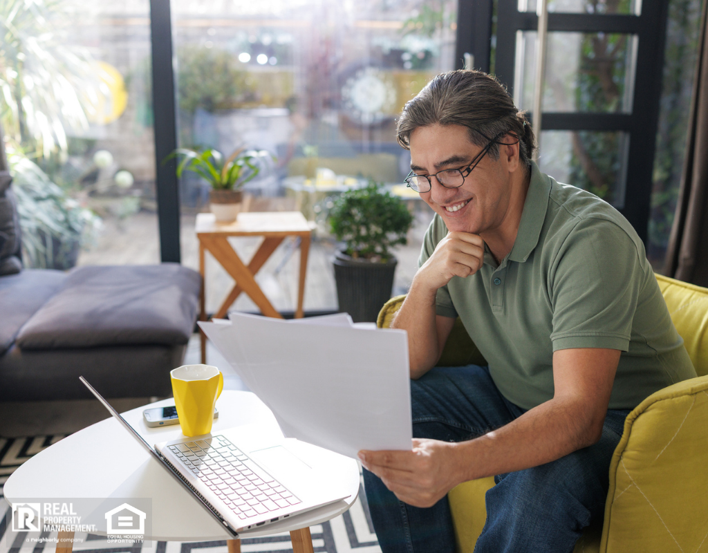 A man sitting in a yellow chair reviewing papers and working on a laptop.