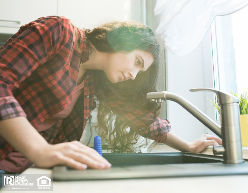 Woman in checkered shirt checking faucet while having problem with dripping faucet in kitchen.