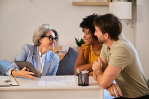 A property manager presenting investment information on a tablet to a young couple during a home consultation.