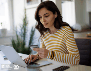 A woman sitting at a table, using a laptop while holding a credit card in her hand.