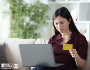 A woman seated on a couch, anxiously holding a credit card, reflecting the tension of a potential rental scam situation.