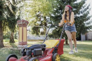 A woman performs summer maintenance by mowing her lawn.