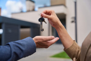 close up of a handing passing over keys in front of a house