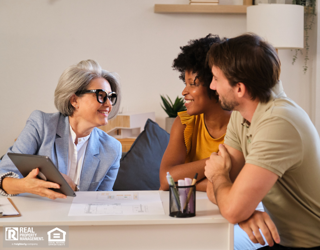 A property manager presenting investment information on a tablet to a young couple during a home consultation.